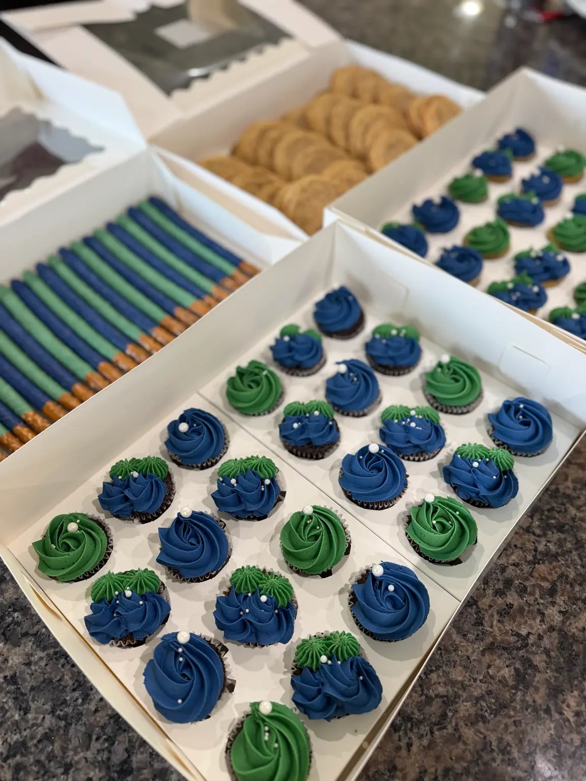 Blue and green mini cupcakes, cupcakes, pretzels and cookies boxed for an event