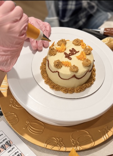Guest piping autumn buttercream details onto a mini cake in a LoveLeigh decorating class