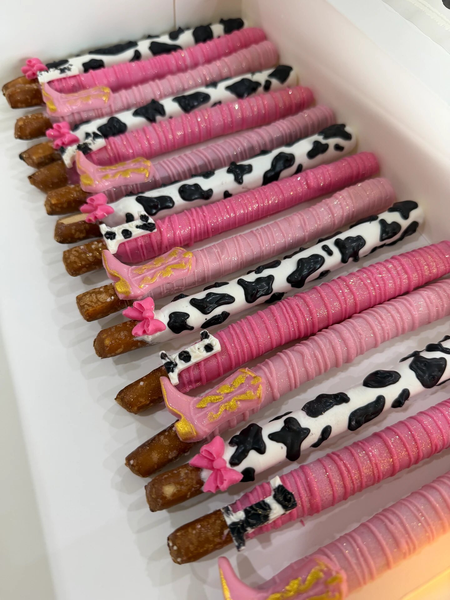 Cowgirl-themed pretzel rods with cow print, pink drizzle, cowboy hats and gold boots