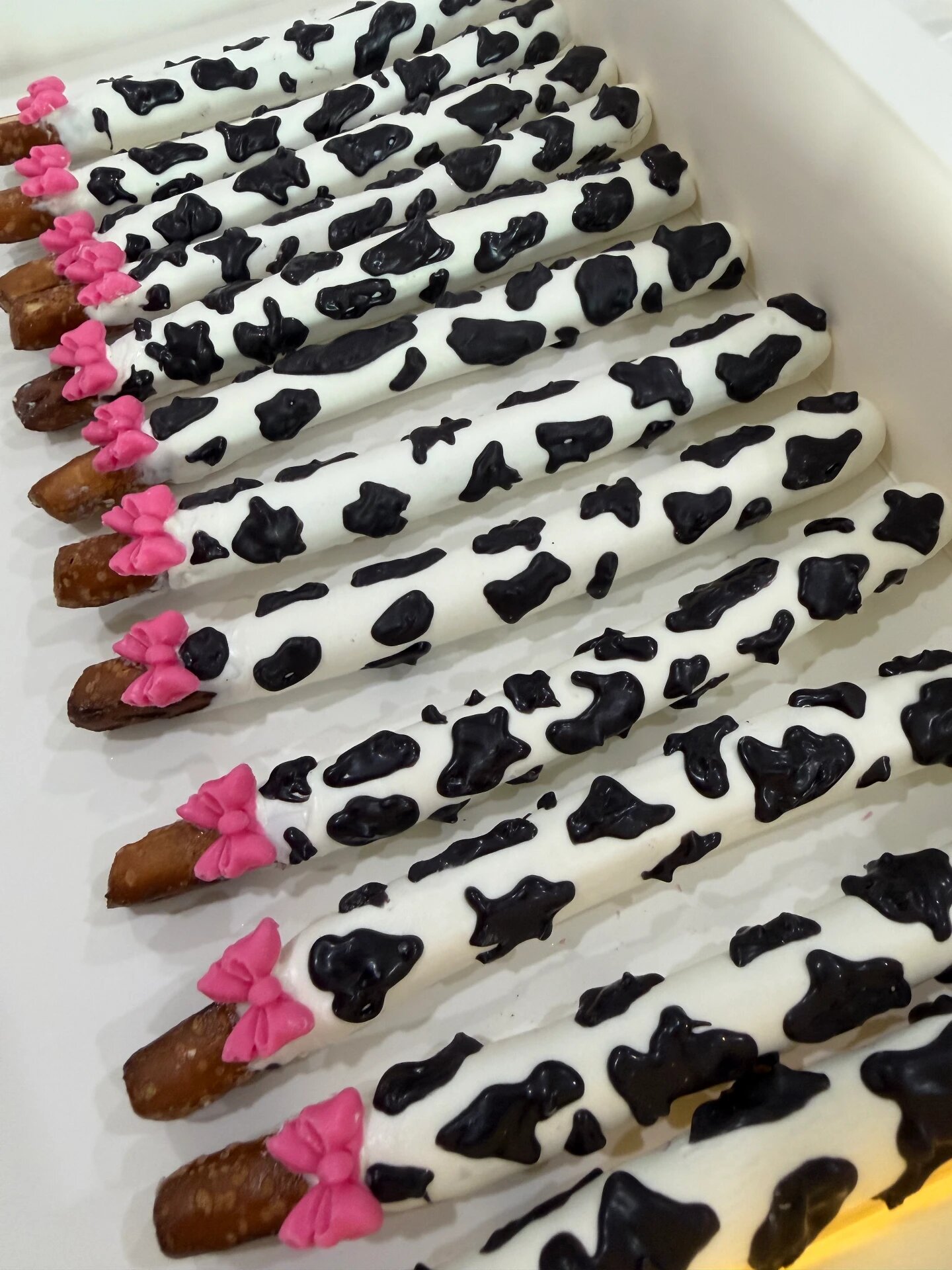 White chocolate pretzel rods with black cow print and pink candy bows